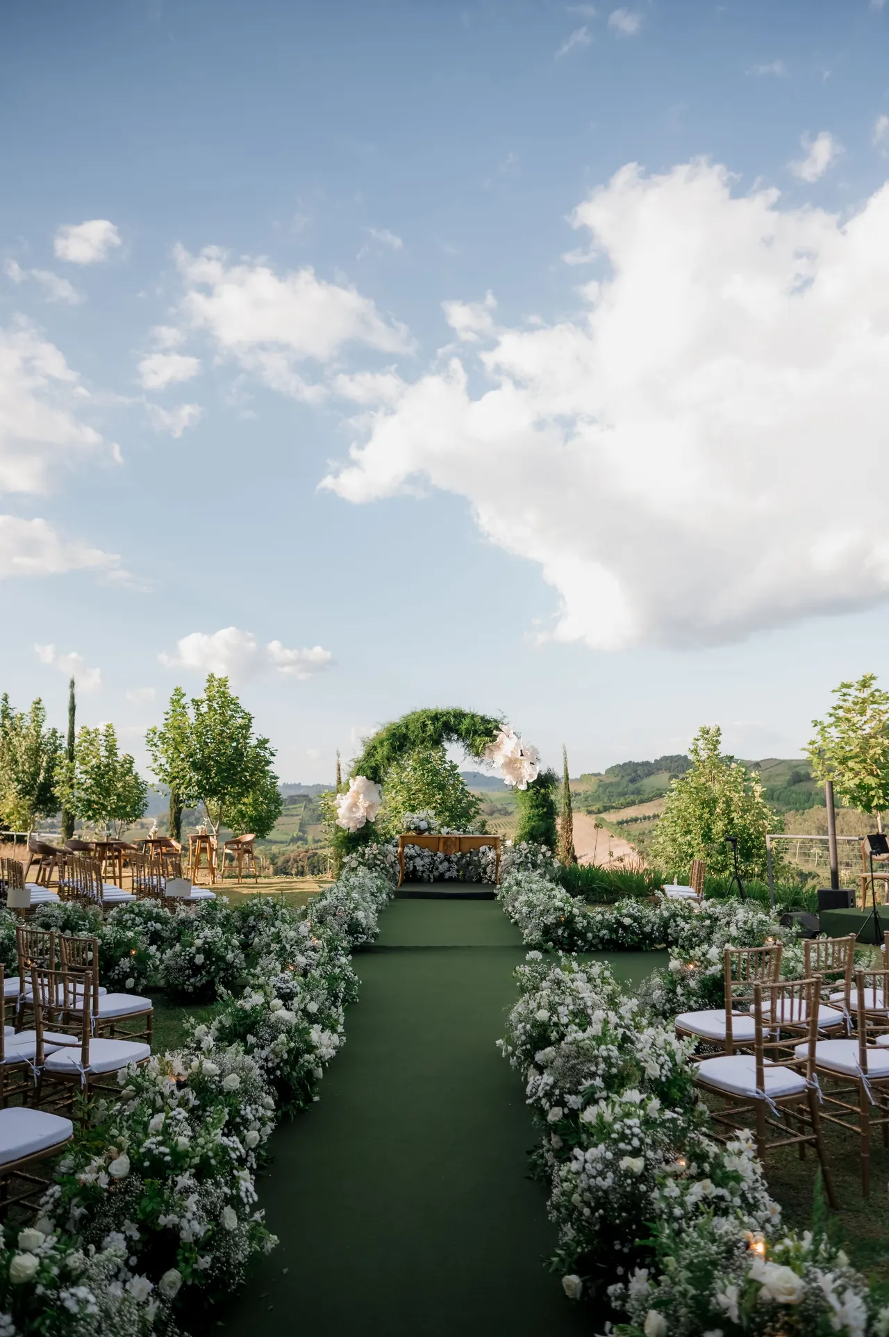 Pasillo de ceremonia al aire libre con arco floral entre viñedos