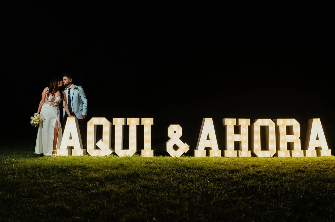 Pareja de noche junto a letras luminosas gigantes en el jardín