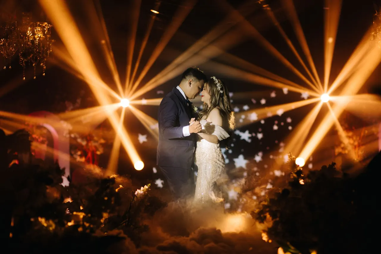 Pareja de novios en su primer baile bajo haces de luz cálida