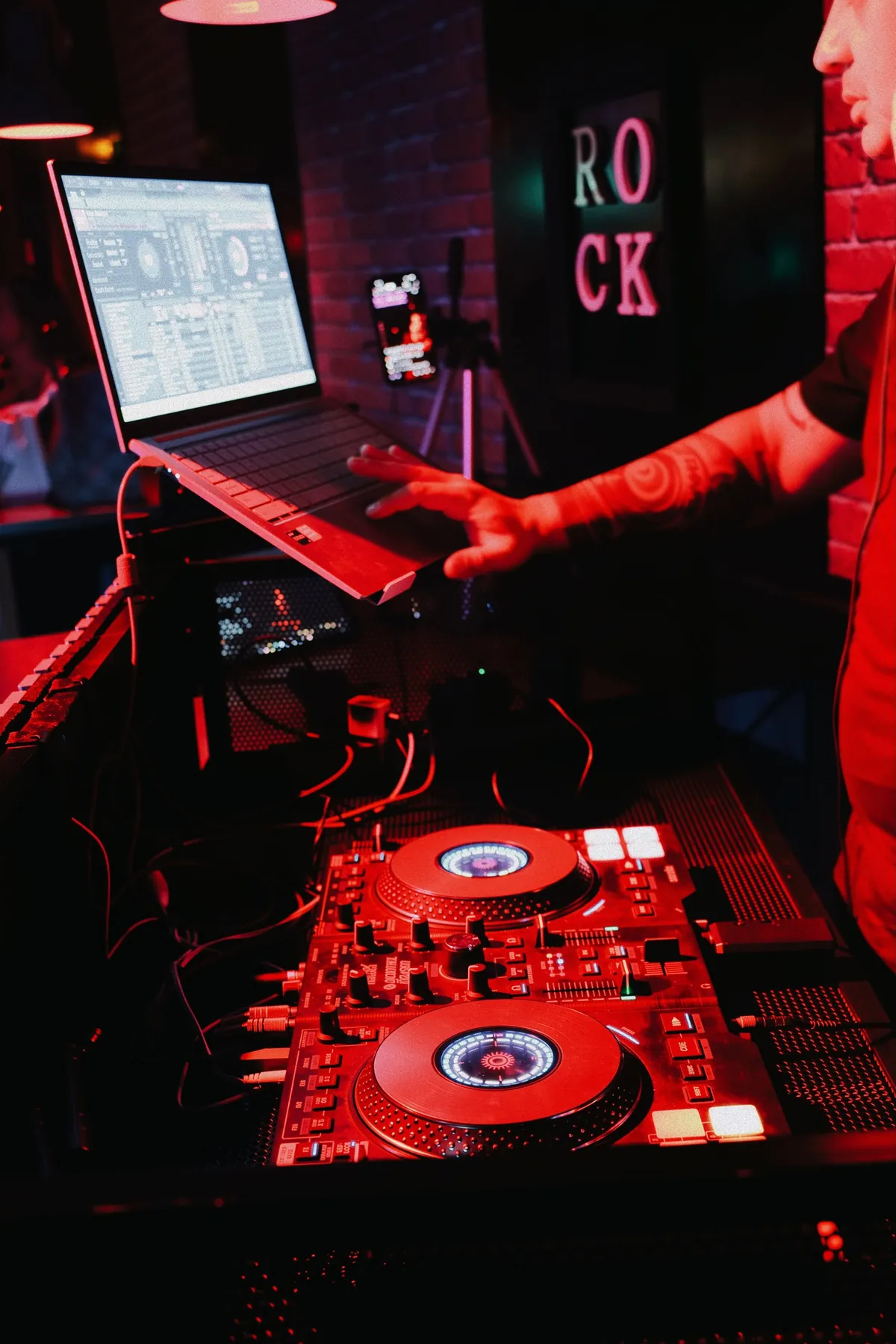 Cabina de DANKO DJ con controladora y portátil bajo luz roja en un club