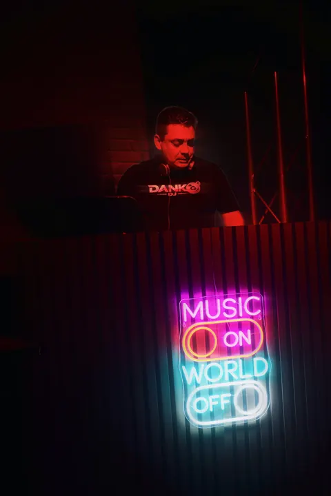 DANKO DJ en cabina bajo el neón «Music On, World Off»
